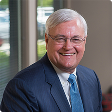 A photo of Bob Adams smiling in a navy suit with a blue tie over a blurred office background